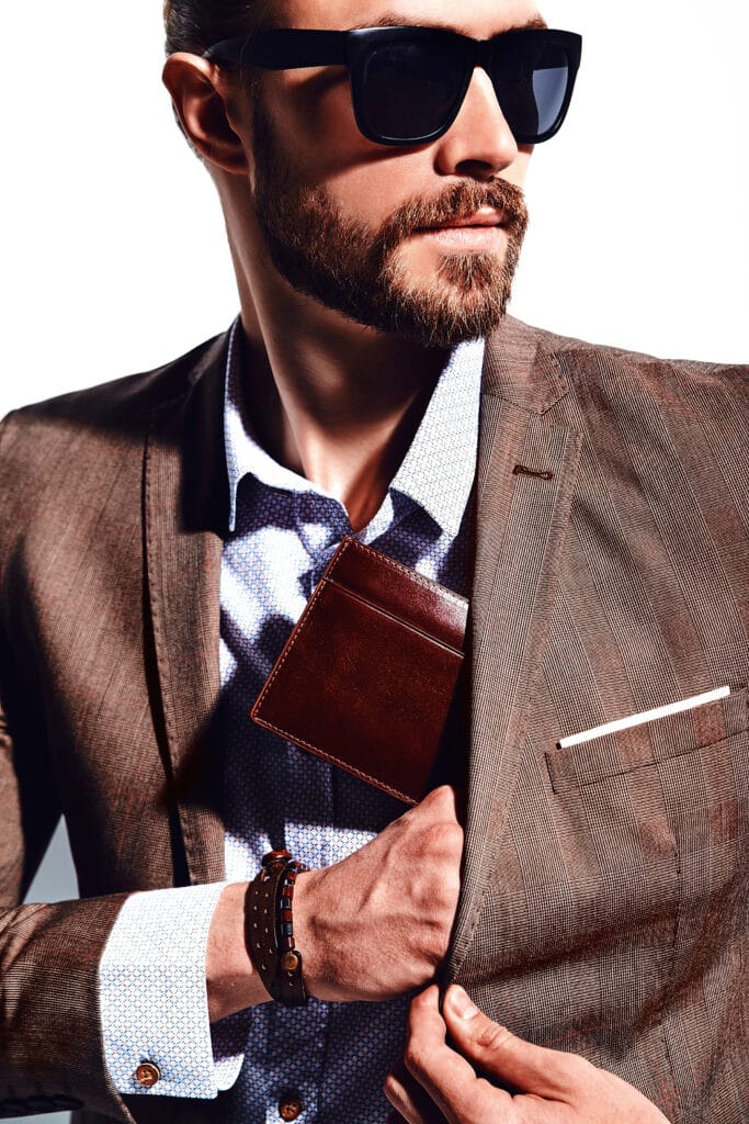 Suits for Fall Fashionable man in sunglasses wearing a brown suit, with a wallet in his pocket, against a white background.