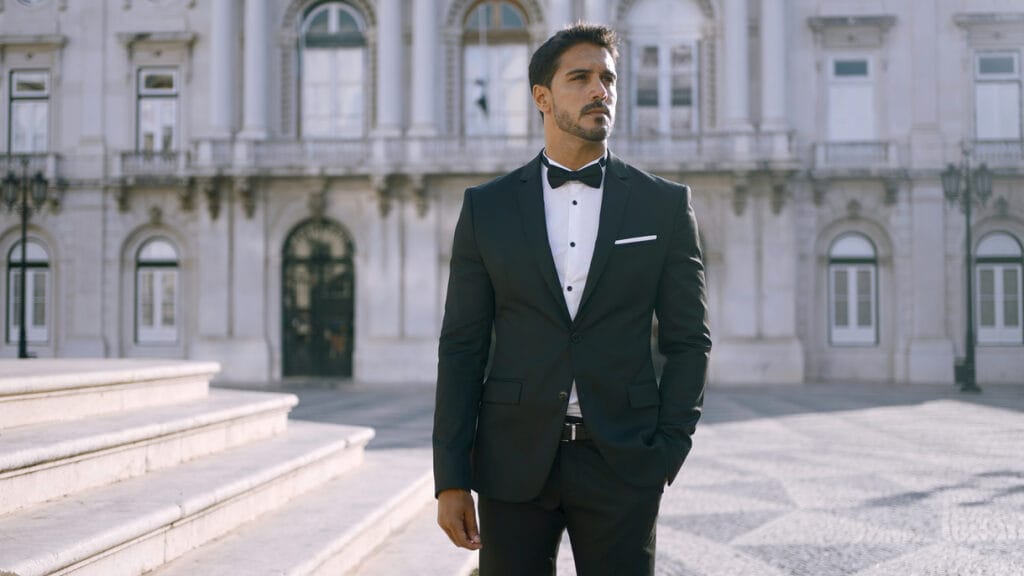 Suit Styling Tips A man in a tuxedo stands confidently in front of a grand building.